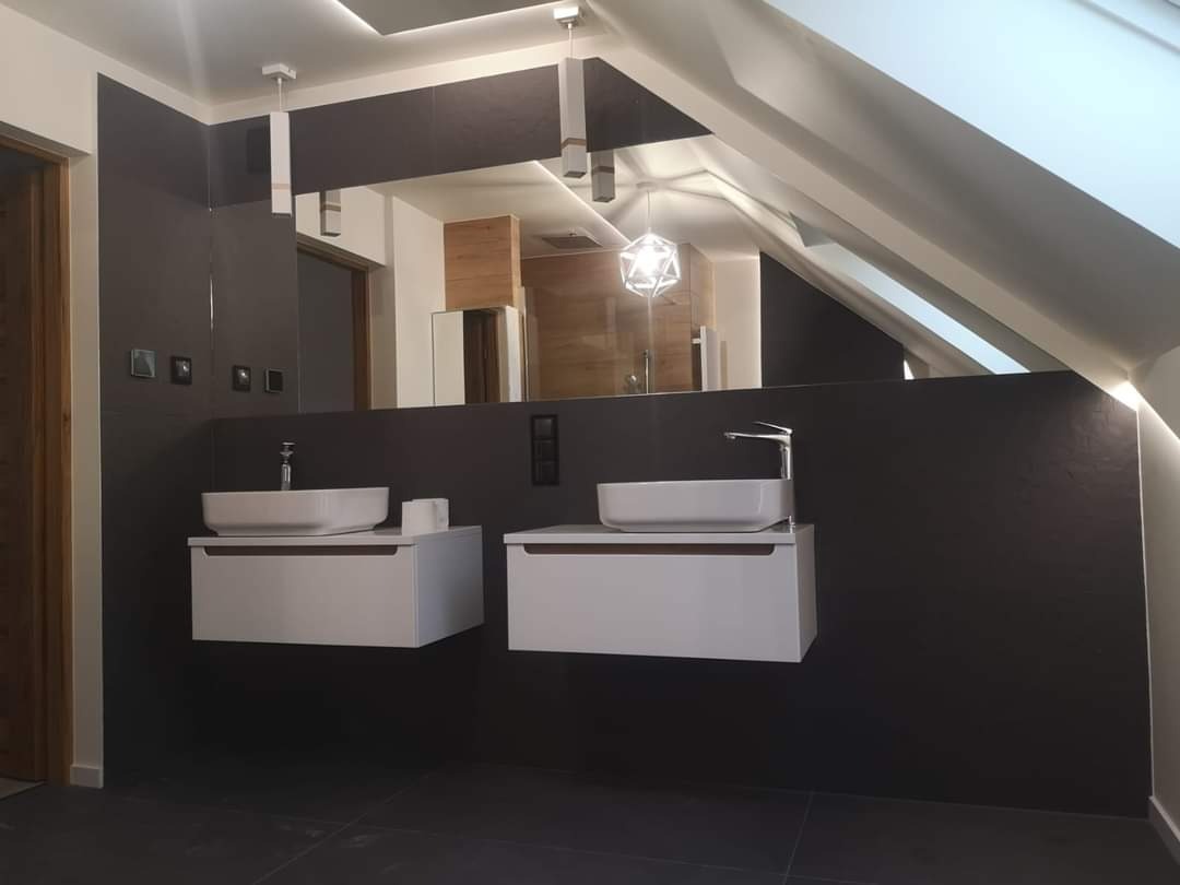 Nowoczesna łazienka na poddaszu z dwoma białymi umywalkami nablatowymi na szafkach, szare ściany z widoczną fakturą, czarne płytki podłogowe i oświetlenie LED.