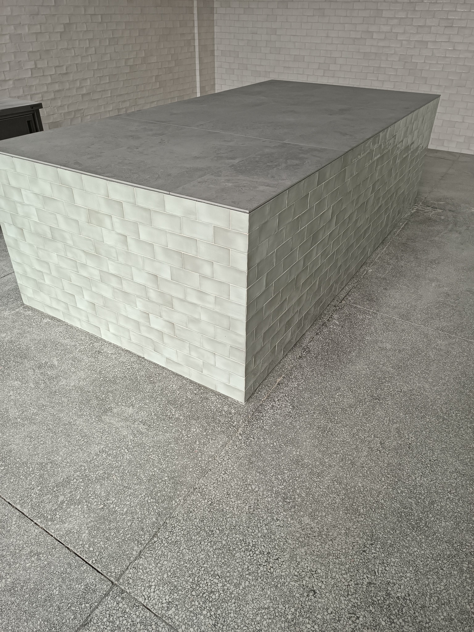 Wyspa kuchenna wykończona jasnymi, prostokątnymi płytkami z szarą, kamienną powierzchnią blatu, widoczna w Bielsku-Białej, z podłogą wyłożoną szarymi płytami z drobnym wzorem.