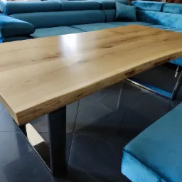 Stolik kawowy z blatem z litego drewna o nieregularnych krawędziach i metalowych nogach, wykonany w Poznaniu, na tle turkusowej sofy.