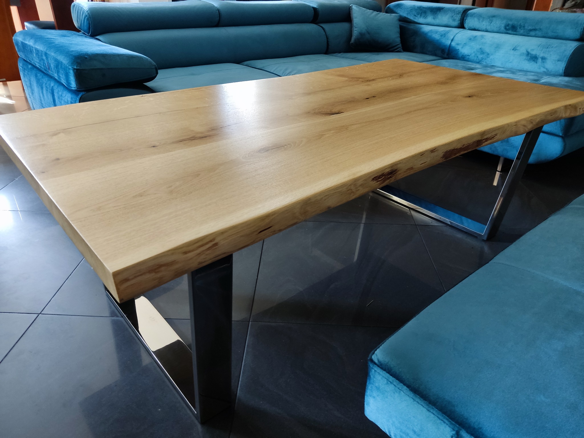 Stolik kawowy z blatem z litego drewna o nieregularnych krawędziach i metalowych nogach, wykonany w Poznaniu, na tle turkusowej sofy.