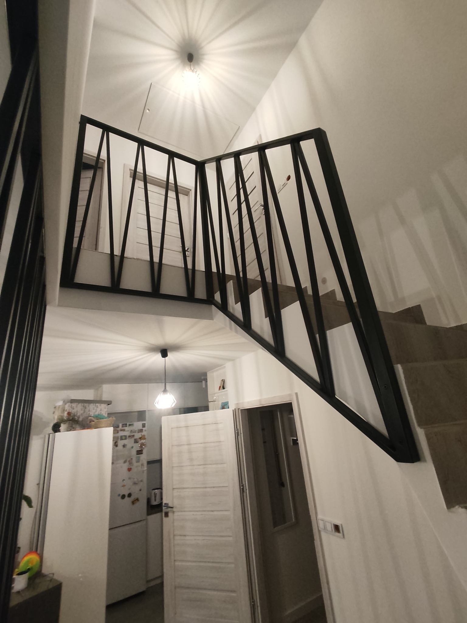 Nowoczesna balustrada schodowa z czarnych, ukośnych prętów, widok z dołu, z fragmentem kuchni w tle.