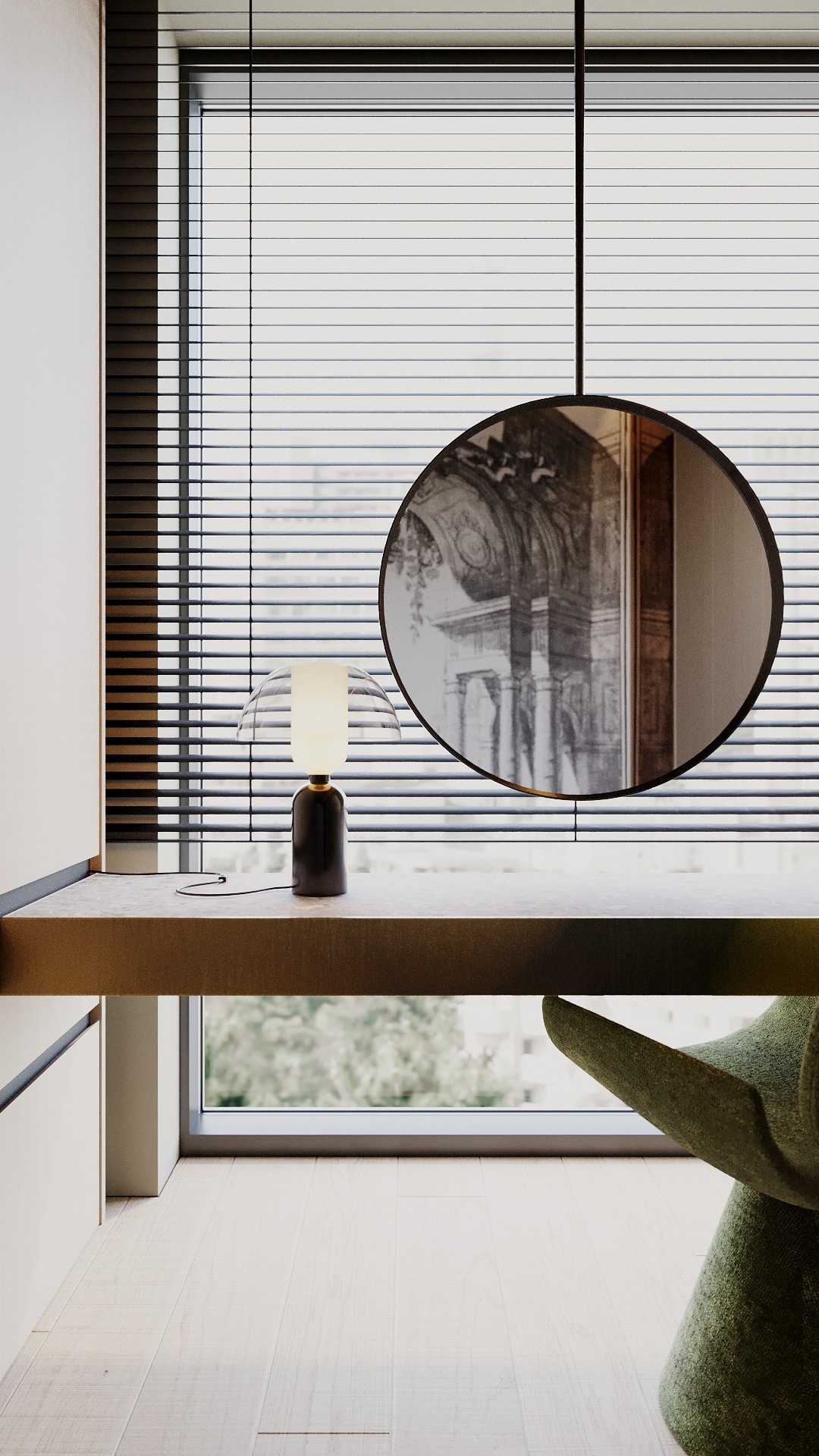 Nowoczesne wnętrze z biurkiem przy oknie z żaluzjami, lampką nocną i okrągłym lustrem odbijającym grafikę architektoniczną, z fragmentem zielonego fotela w kadrze.
