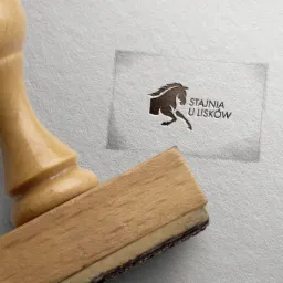 Stempel drewniany z odciśniętym logotypem konia i napisem 'Stajnia u Lisków' na teksturowanym papierze.
