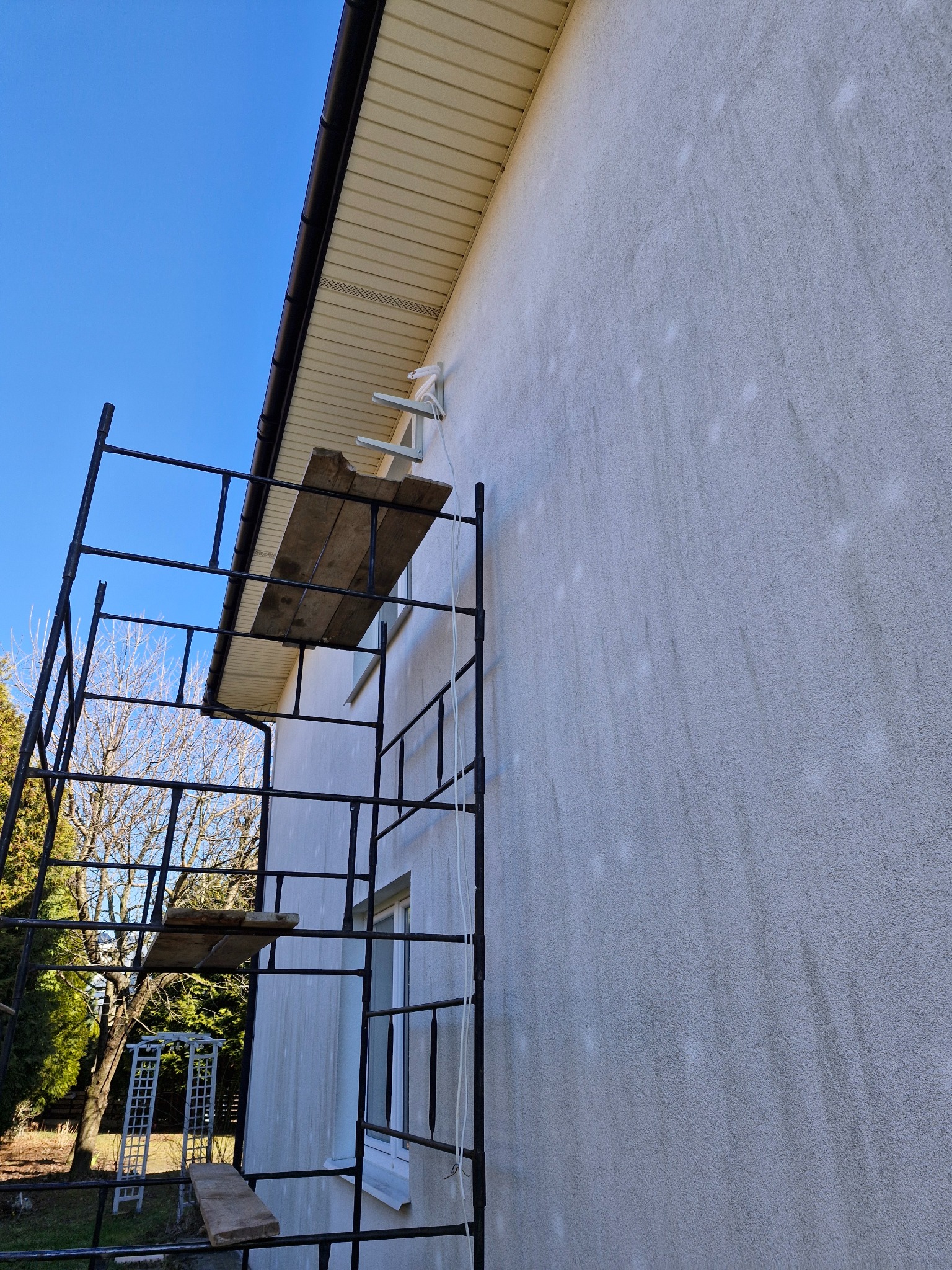 Elewacja budynku w trakcie czyszczenia, widoczne ślady po myciu ciśnieniowym, rusztowanie przy ścianie, uchwyty klimatyzacji na ścianie pod okapem.