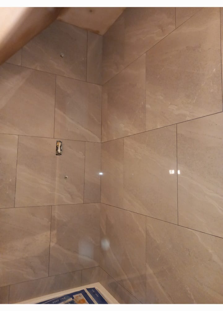 Ściana łazienki wyłożona beżowymi płytkami imitującymi marmur, widoczne otwory na armaturę i zabezpieczona wanna.