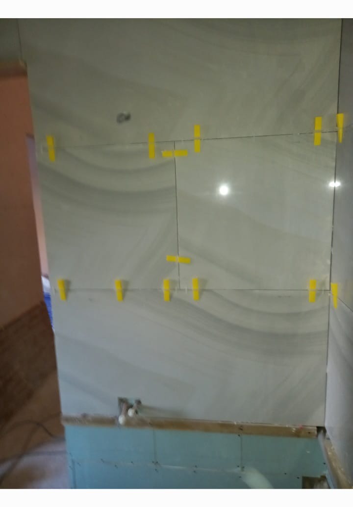 Ściana z ułożonymi płytkami ceramicznymi z użyciem żółtych krzyżyków dystansowych, widoczne niedokończone prace przy dolnej krawędzi ściany.