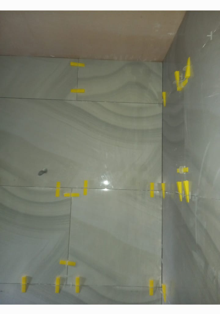 Świeżo ułożone, szare płytki imitujące marmur na ścianie z użyciem żółtych krzyżyków dystansowych.