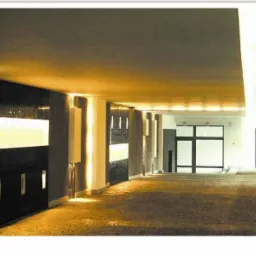 Nowoczesne wnętrze biurowe z oświetleniem LED w ścianach, widok na przeszklone drzwi wejściowe, brązowa podłoga.