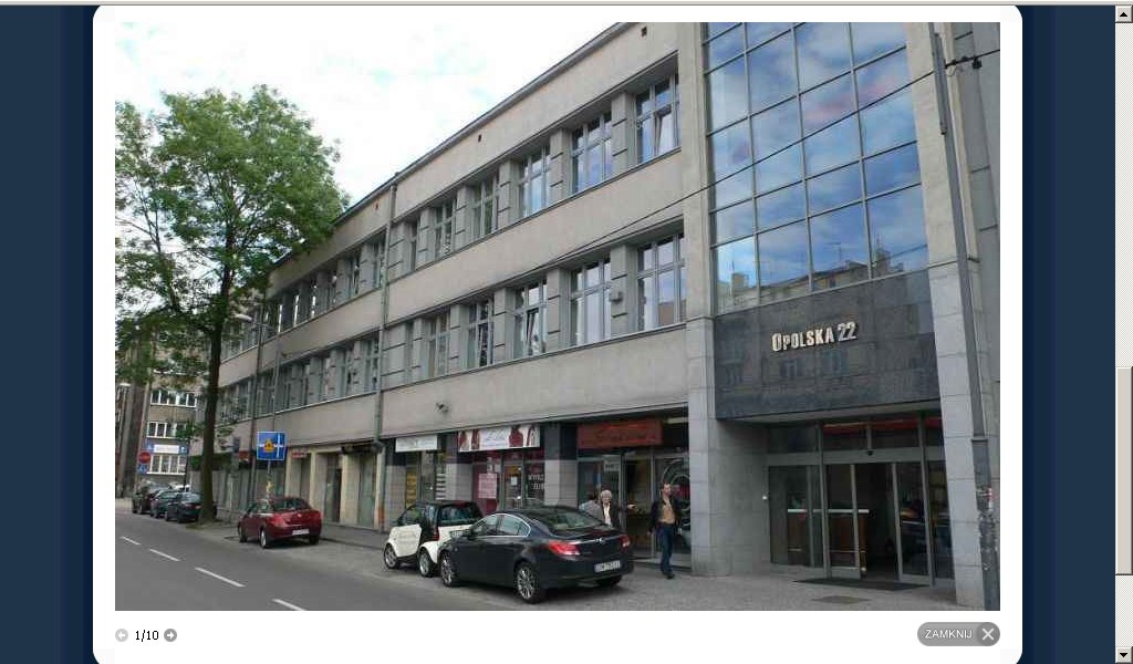 Szary budynek biurowy z dużą szklaną fasadą, oznaczony adresem Opolska 22, z zaparkowanymi samochodami i przechodniami na chodniku.