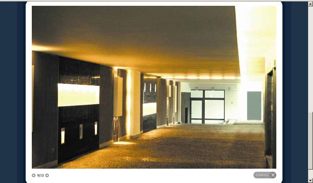 Nowoczesne wnętrze biurowe z oświetleniem LED w ścianach, widok na przeszklone drzwi wejściowe, brązowa podłoga.