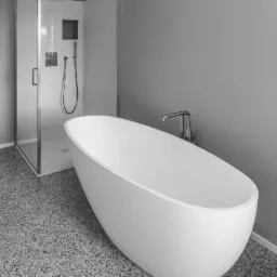 Nowoczesna łazienka w odcieniach szarości z wolnostojącą białą wanną i przeszkloną kabiną prysznicową z chromowaną armaturą.