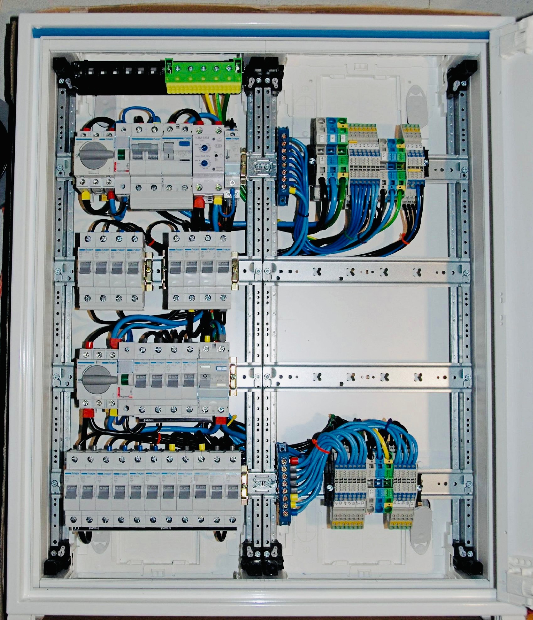 Wnętrze rozdzielnicy elektrycznej z zamontowanymi bezpiecznikami, wyłącznikami różnicowoprądowymi i listwami zaciskowymi, uporządkowane przewody w kolorach niebieskim, czarnym, żółto-zielonym,...