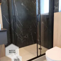 Kabina prysznicowa z czarnymi profilami i marmurowymi płytkami w tle, widoczna toaleta w Gnieźnie.