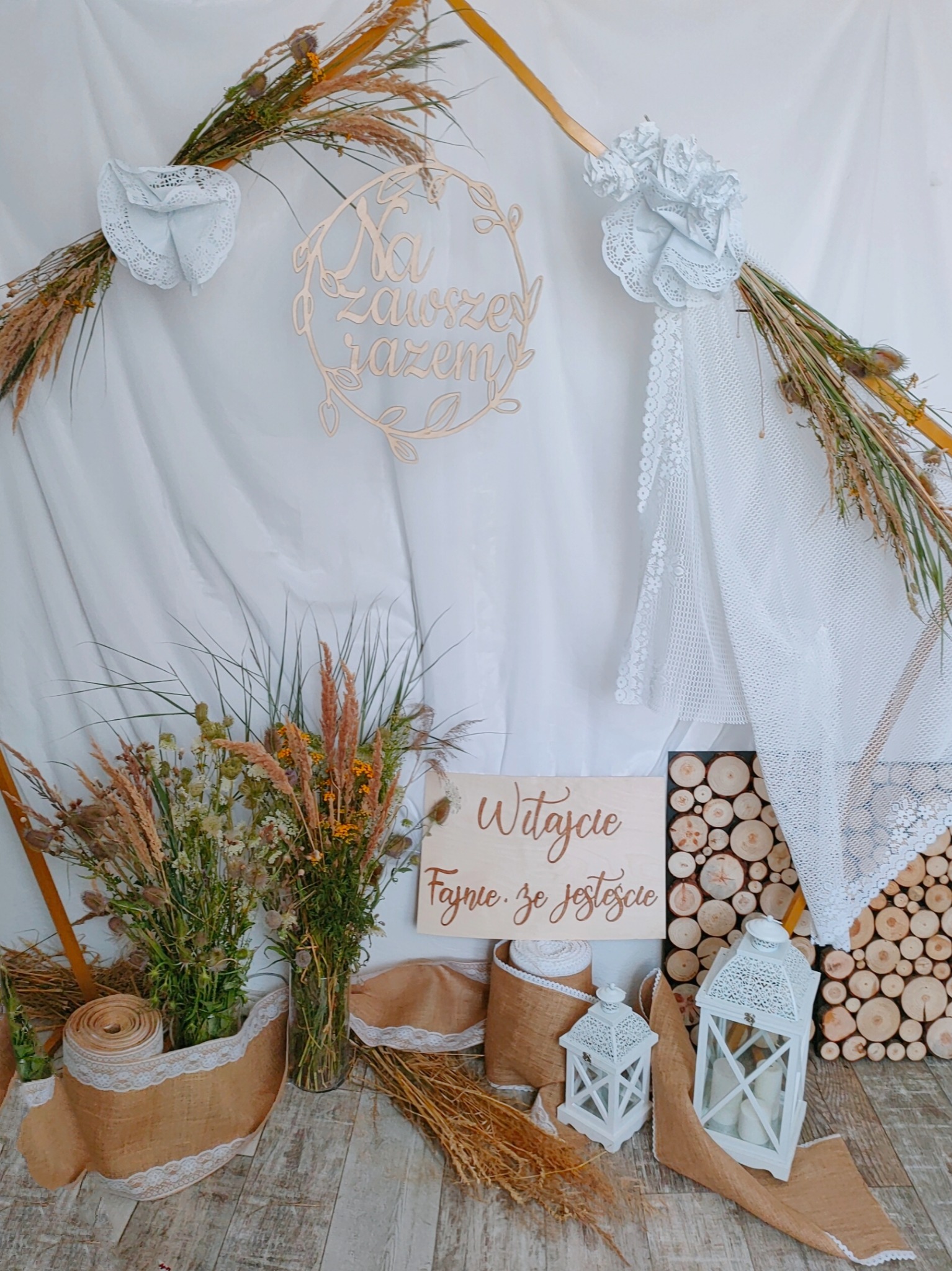 Dekoracja ślubna w stylu rustykalnym z drewnianym napisem 'Na zawsze razem', kompozycjami z traw i kwiatów polnych, lampionami i drewnianymi plastrami