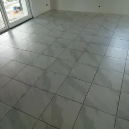 Ułożone płytki podłogowe imitujące marmur w nowym, jasnym pomieszczeniu z dużym oknem przesuwnym wychodzącym na piaskownicę z zabawkami.