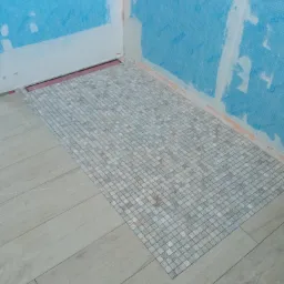 Układanie mozaiki w strefie prysznicowej, widoczne zabezpieczenie przeciwwilgociowe ścian folią w płynie, odpływ liniowy w posadzce.