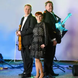 Trzyosobowy zespół pozuje na scenie w formalnych strojach: skrzypek z lewej, gitarzysta z prawej i wokalistka pośrodku w czarnej, ażurowej sukience.