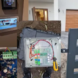 Montaż automatyki do bram: skrzynka sterownicza z okablowaniem i płytką drukowaną, widok na monitor wideodomofonu z podglądem posesji oraz fragment bramy w tle.