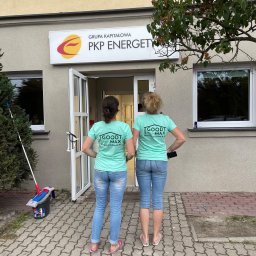 Goodmax Khrystyna Stakhiv - Dwie kobiety w jeansach i turkusowych koszulkach firmowych stoją przed budynkiem PKP Energetyka, obok widoczne wiadro i mop do podłogi.