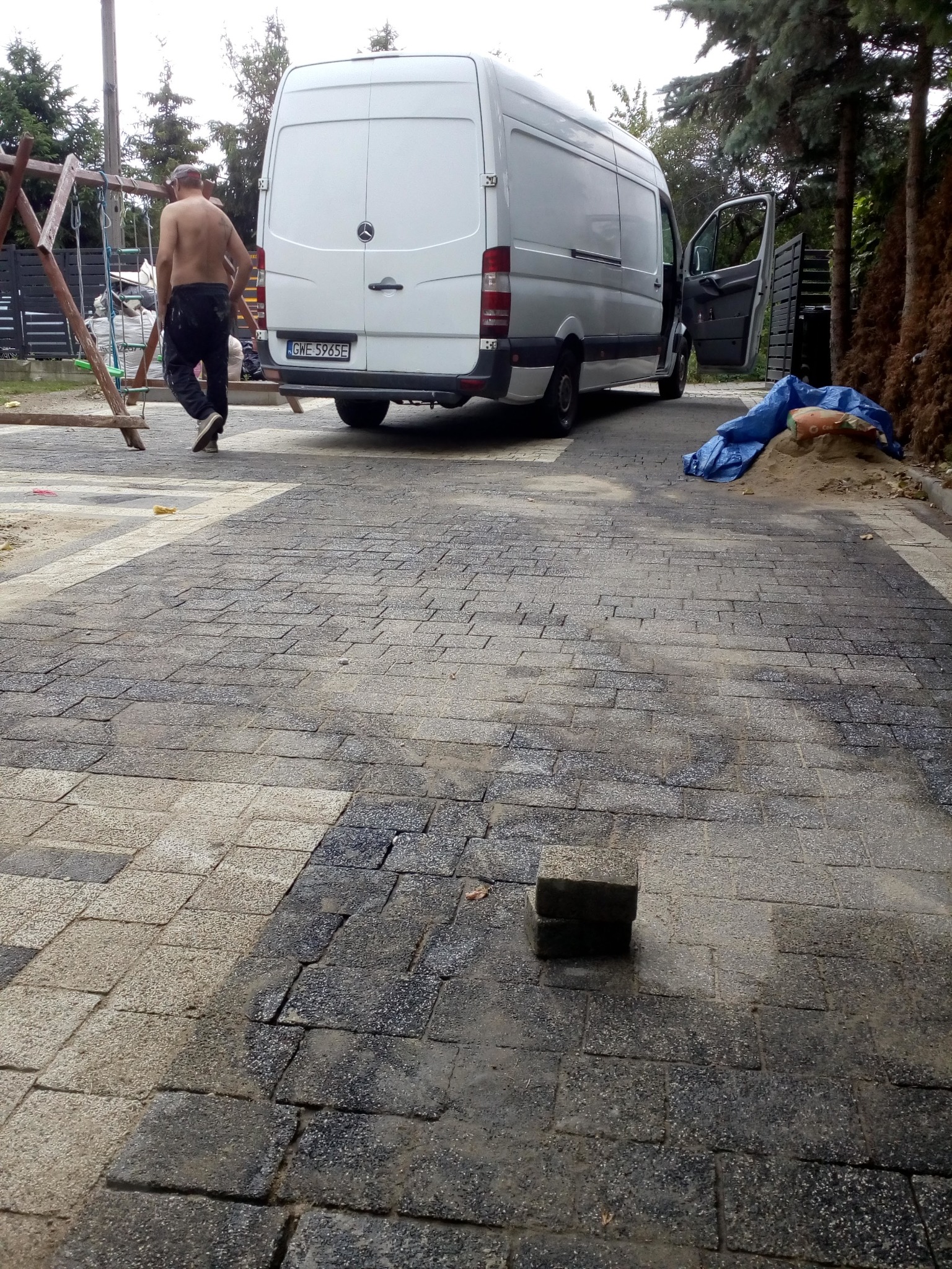 Niedokończona nawierzchnia z kostki brukowej w Redzie, z widocznym samochodem dostawczym Mercedes Sprinter i pracownikiem bez koszulki w tle, obok placu zabaw.