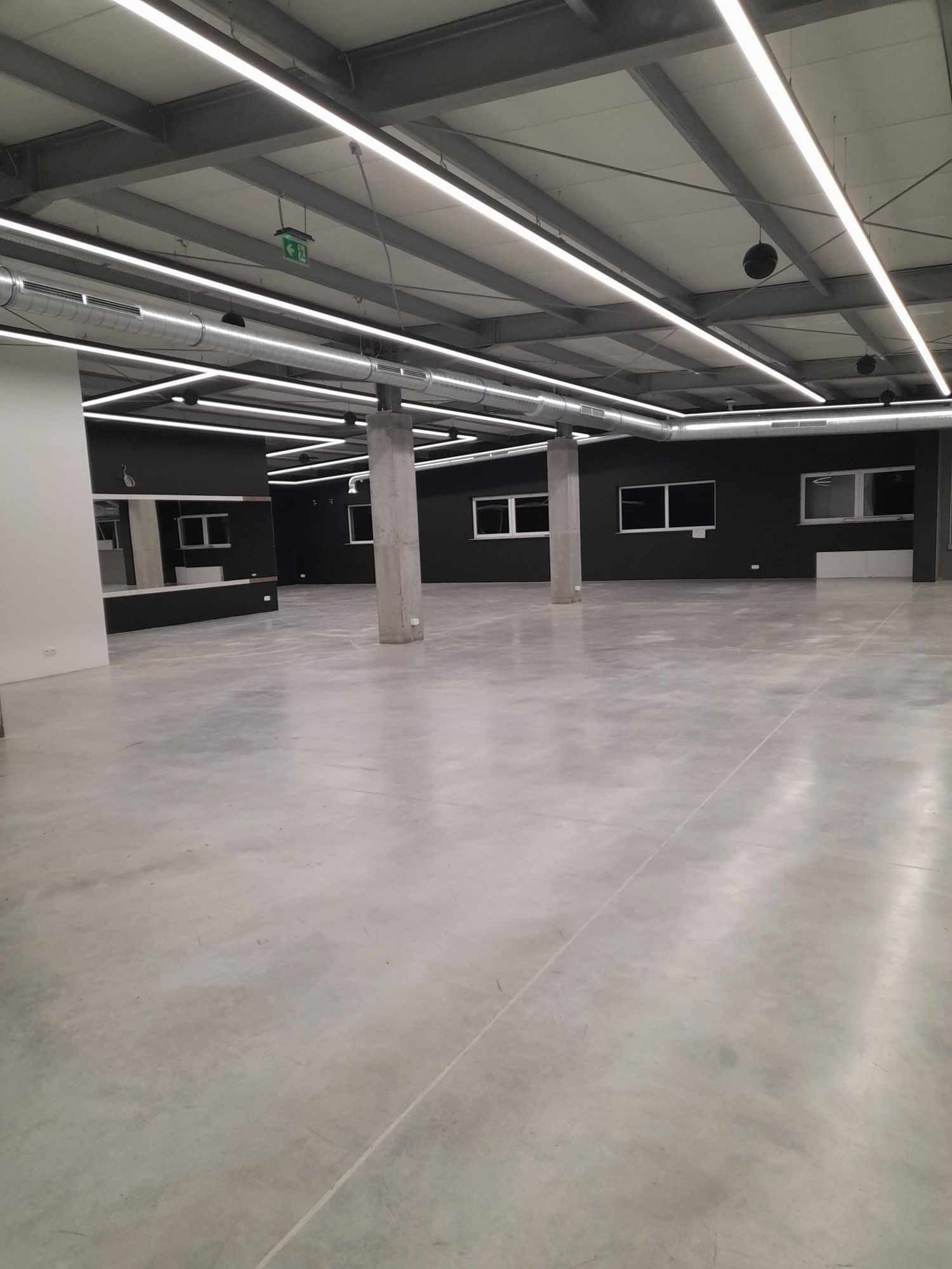 Przestronne, puste wnętrze biurowe z betonową podłogą, oświetleniem LED i surowymi, metalowymi elementami konstrukcyjnymi