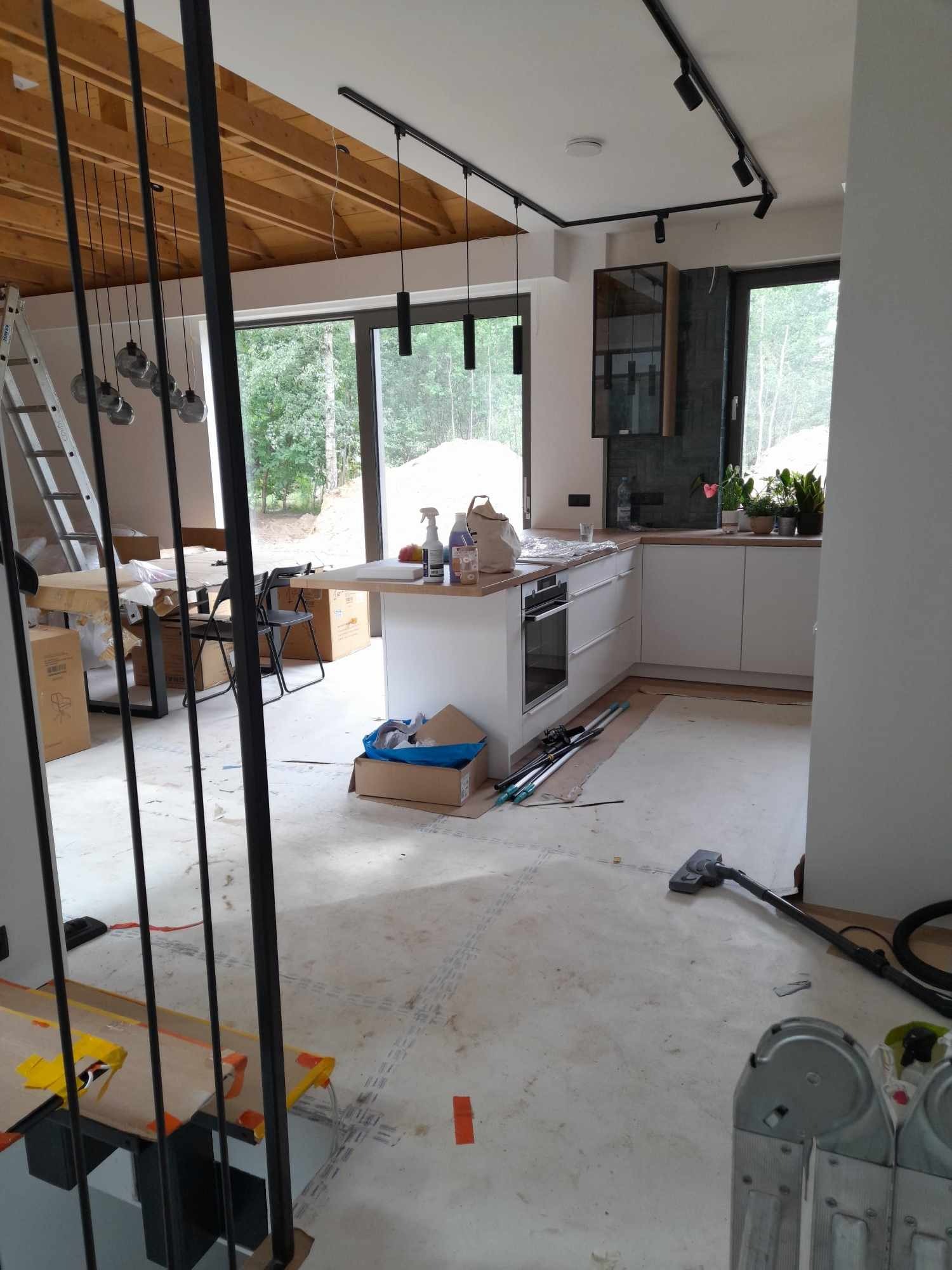 Wnętrze kuchni w trakcie wykańczania, widoczne kartony, narzędzia i odkurzacz, surowy beton na podłodze, na blacie środki czystości i jabłko.