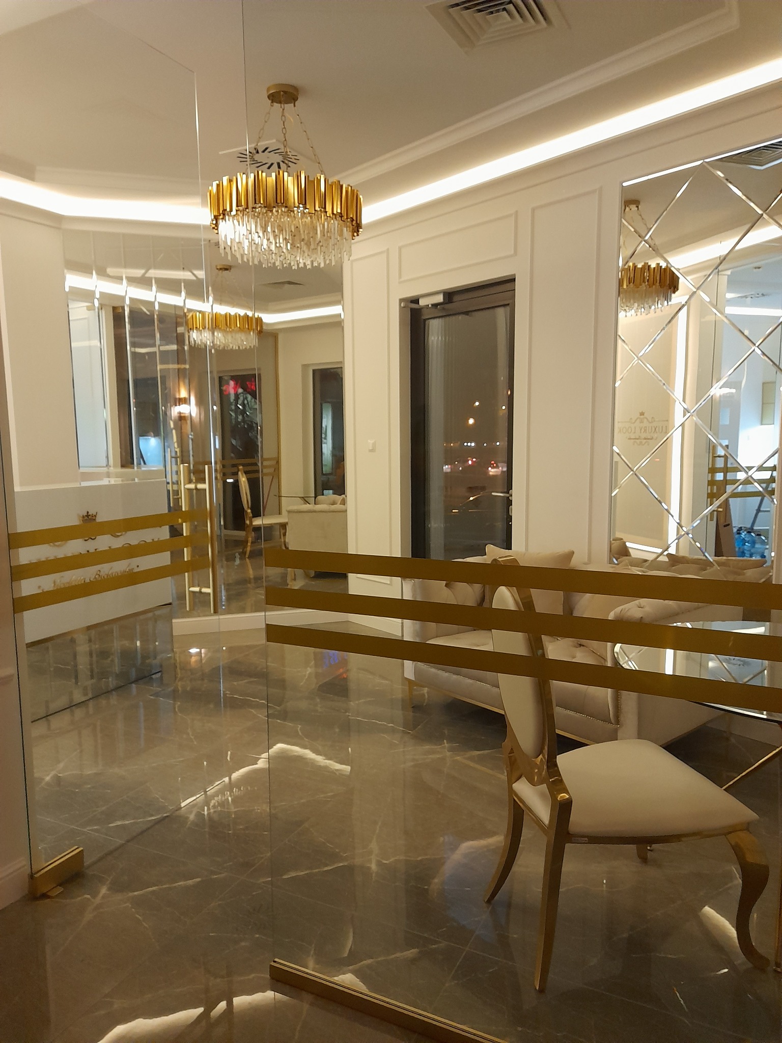 Eleganckie wnętrze biura z marmurową podłogą, złotym żyrandolem i szklanymi drzwiami z ozdobnymi detalami.