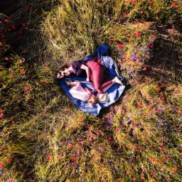 Widok z góry na kobietę i dziecko leżące na piknikowym kocu w kwitnącym polu maków i chabrów, z kapeluszem obok dziecka, uchwycony z drona.