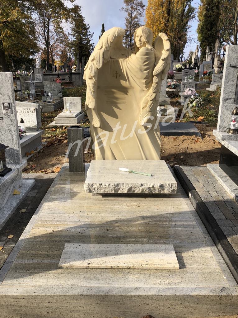 Jasny, granitowy pomnik z rzeźbą anioła z rozłożonymi skrzydłami, pojedynczy, biały kwiat na płycie, cmentarz w tle.