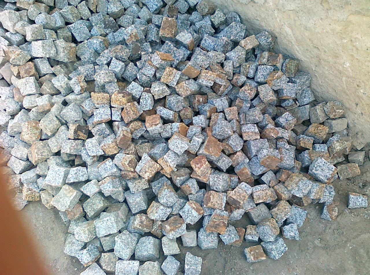 Kupa szaro-brązowej kostki granitowej o nieregularnych kształtach, leżąca na ziemi, gotowa do ułożenia. Widok z góry.