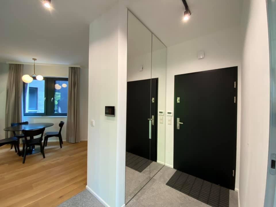 Nowoczesne wnętrze mieszkania z parkietem, czarnym okrągłym stołem z krzesłami, lustrzaną ścianą odbijającą drzwi wejściowe i czarne drzwi wewnętrzne.