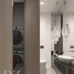 Elegancka łazienka z pralką i suszarką ukrytą za drewnianymi drzwiami, kryształowe żyrandole nad umywalką, czarny blat z pionowymi żłobieniami, lustro odbijające świece.