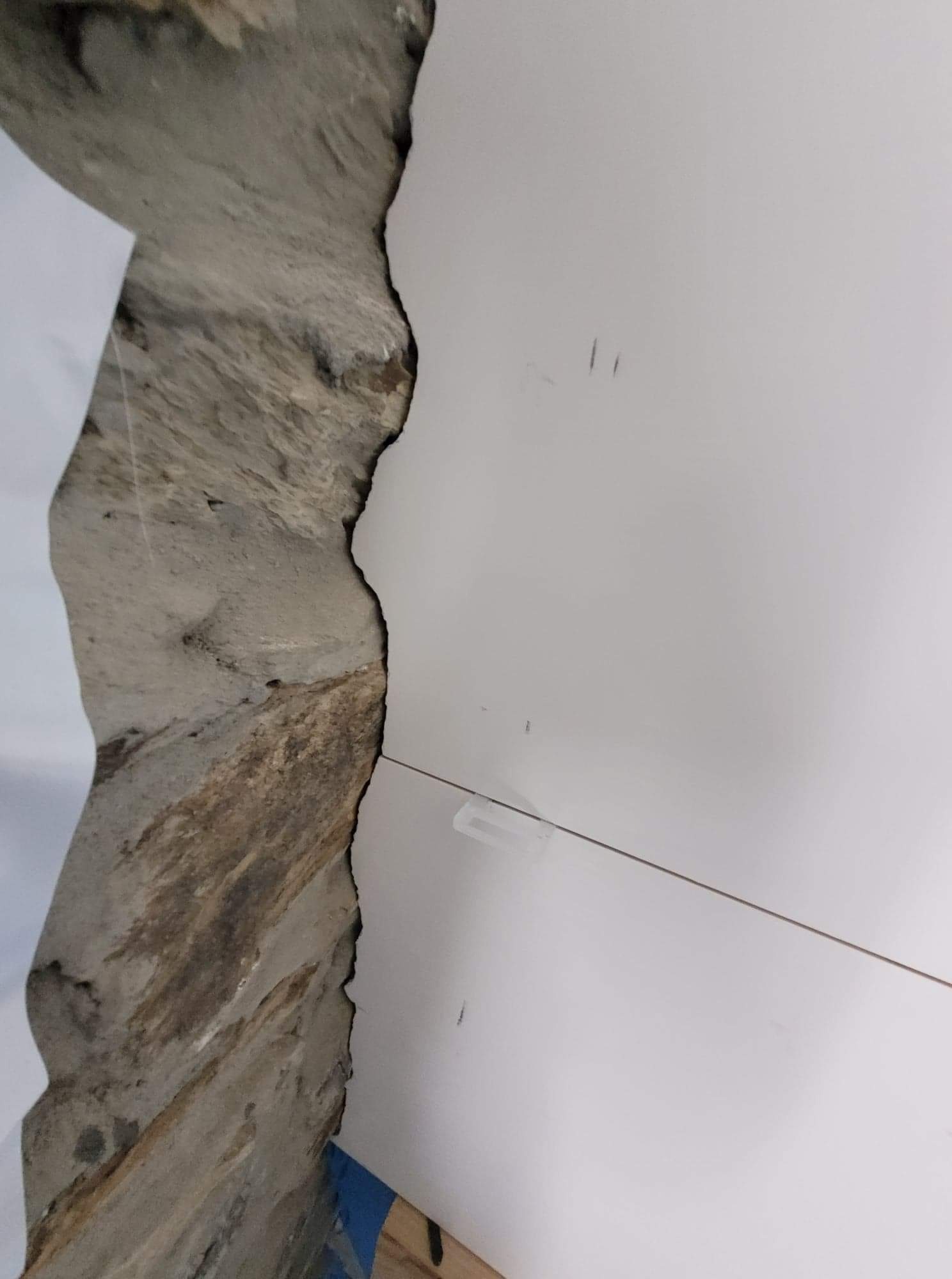 Fragment ściany z surowym betonem sąsiadującym z białą płytą gipsowo-kartonową, widoczne drobne niedoskonałości na powierzchni płyty.