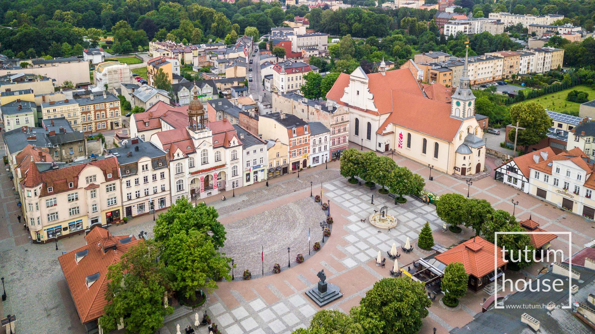 Panorama Rynku w Chojnicach z lotu ptaka, widoczny kościół, ratusz i zabytkowa zabudowa, w rogu logo firmy Tutum House.