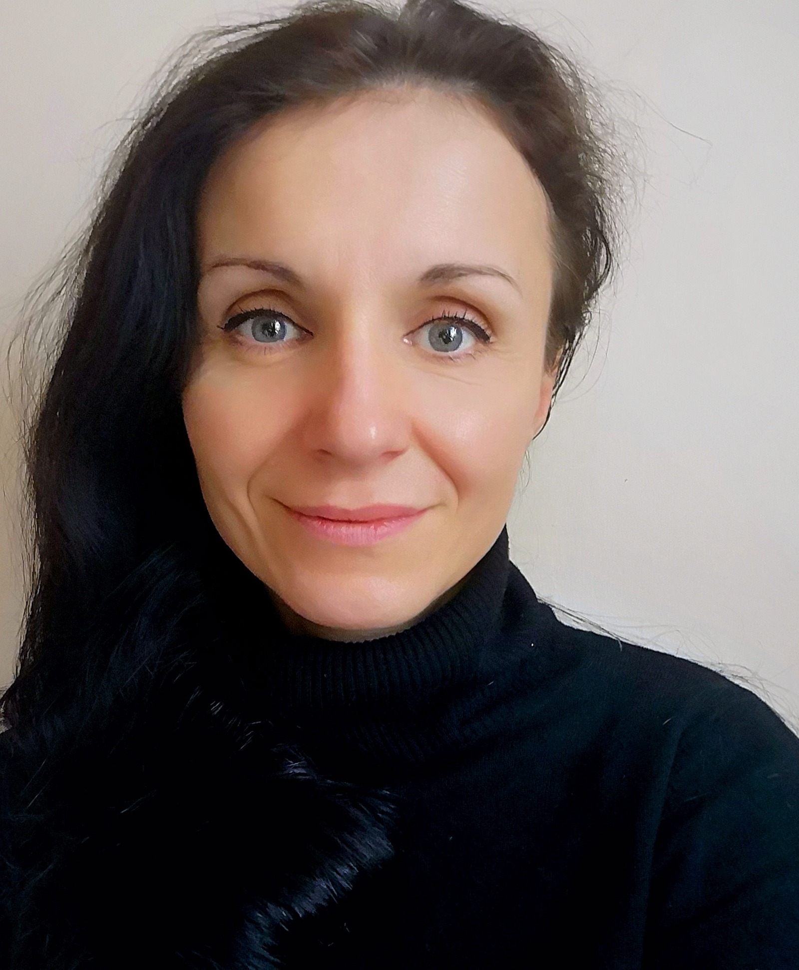 Portret uśmiechniętej kobiety o niebieskich oczach i ciemnych włosach, ubrana w czarny golf.