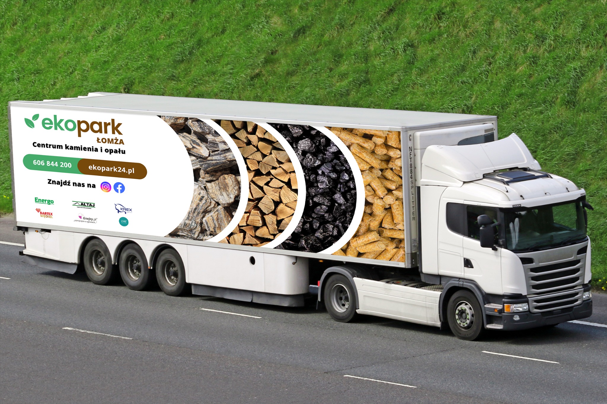 Ciężarówka z reklamą firmy EkoPark Łomża prezentującą kamień, drewno opałowe, węgiel i pellet na naczepie, jadąca po asfalcie na tle zieleni.