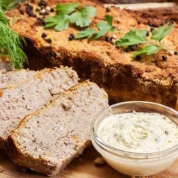 Keks pasztetowy z sosem czosnkowym w szklanej miseczce, udekorowany koperkiem i pietruszką, posypany ziarnami pieprzu, na drewnianej desce.