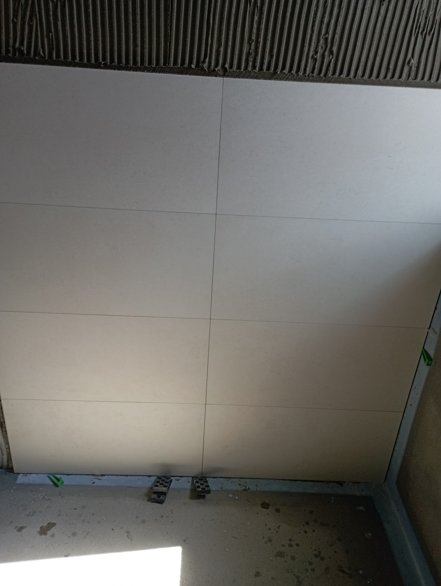 Świeżo ułożone, jasne płytki ścienne z widocznymi krzyżykami dystansowymi i resztkami kleju na górnej krawędzi, ukazujące etap prac wykończeniowych.