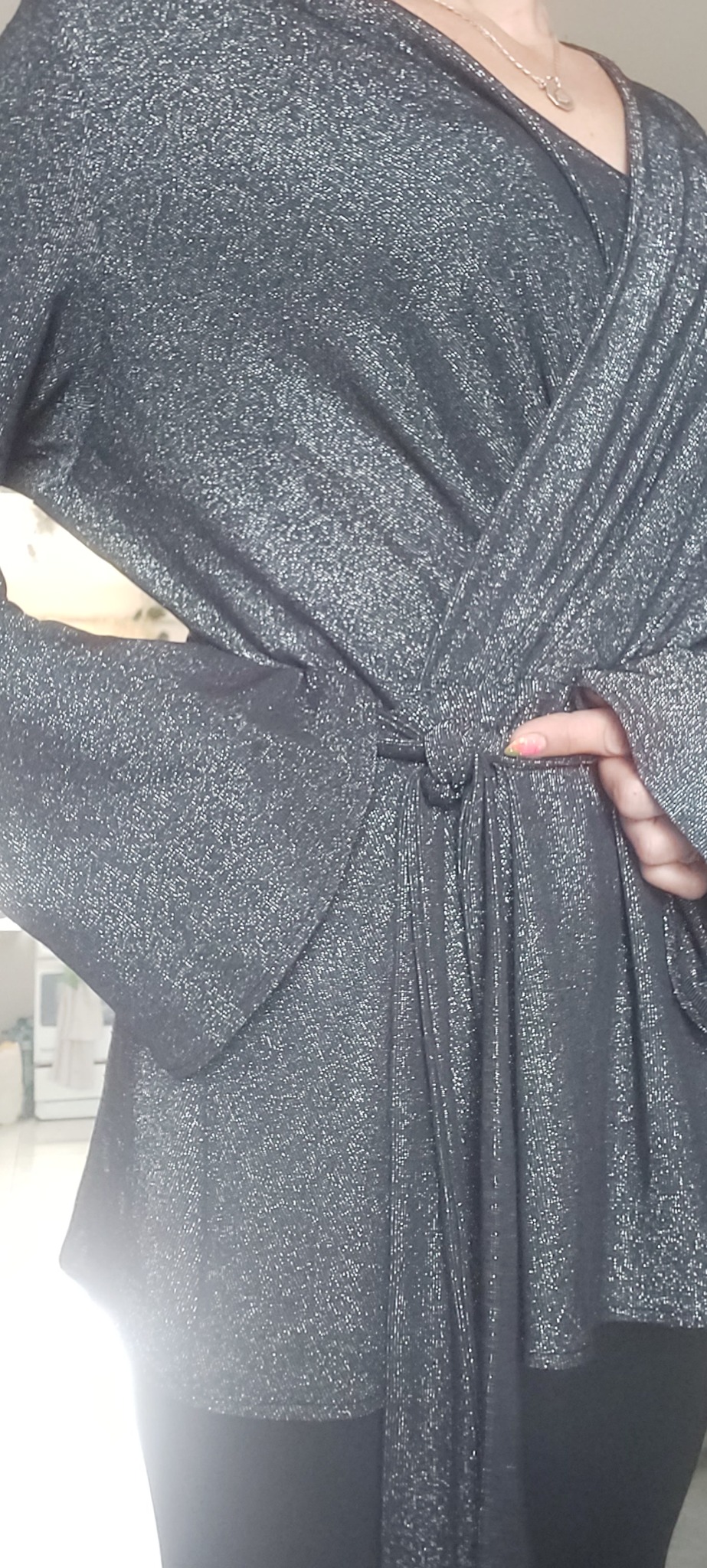 Błyszcząca, drapowana bluzka damska z wiązaniem w talii, prezentowana na osobie, widoczne detale materiału i rękaw