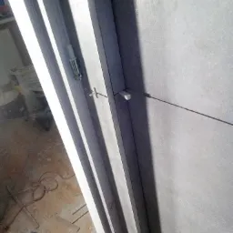 Szare płytki ścienne w trakcie układania, widoczne krzyżyki dystansowe i poziomica laserowa, na podłodze narzędzia.