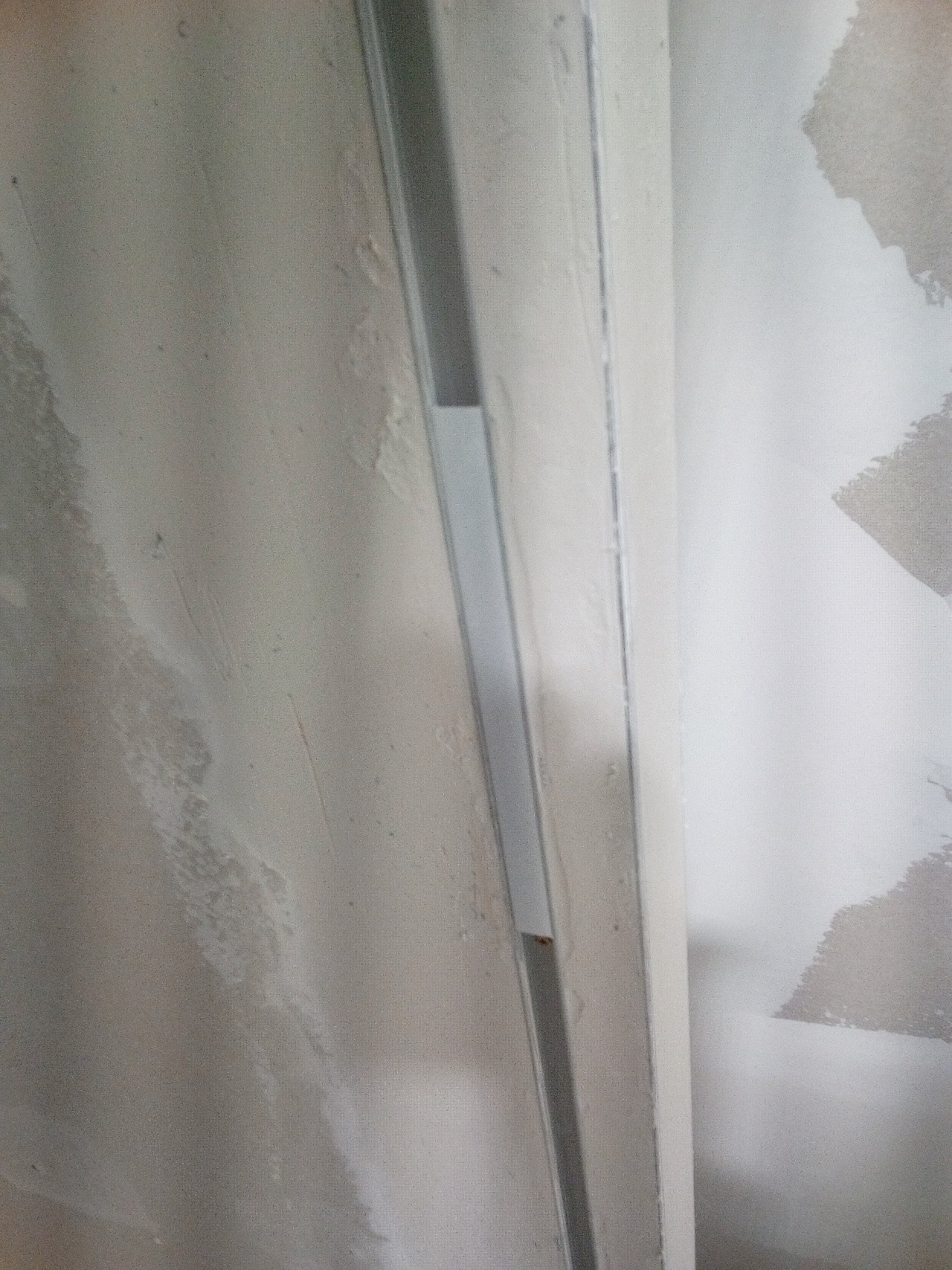 Metalowy profil przymocowany do ściany z widocznymi śladami po gładzi, przygotowanie do dalszych prac wykończeniowych.