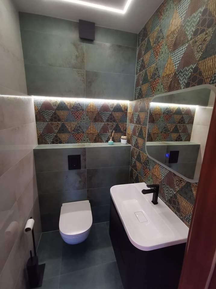 Nowoczesna łazienka z geometrycznymi płytkami, podświetleniem LED, umywalką nablatową i wiszącą toaletą.