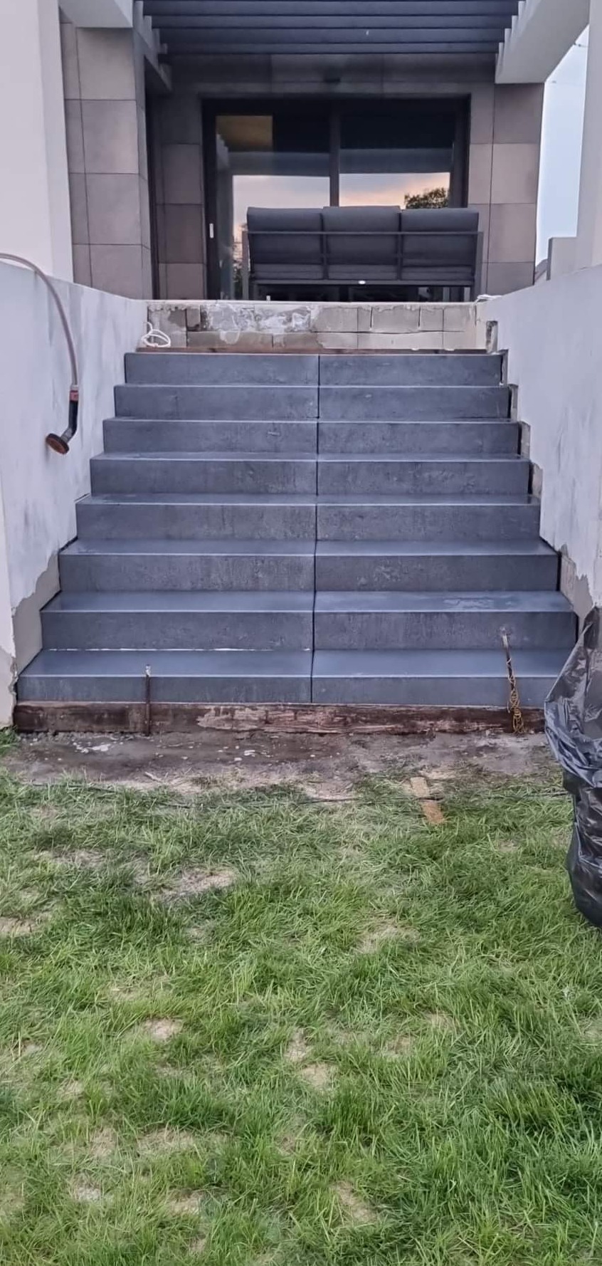 Nowe, szare schody granitowe prowadzące do domu, widok z poziomu trawnika, w trakcie prac wykończeniowych.