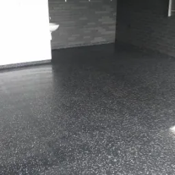 Błyszcząca, ciemnoszara podłoga z drobnymi, jasnymi plamkami w garażu z szarą cegłą i białymi płytkami na ścianach. Na półce drewniane skrzynki.