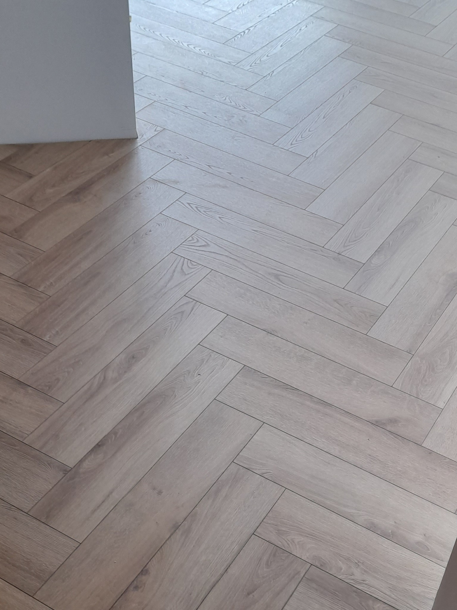 Jasne panele ułożone w jodełkę, widok z góry przy ścianie, imitacja drewna.