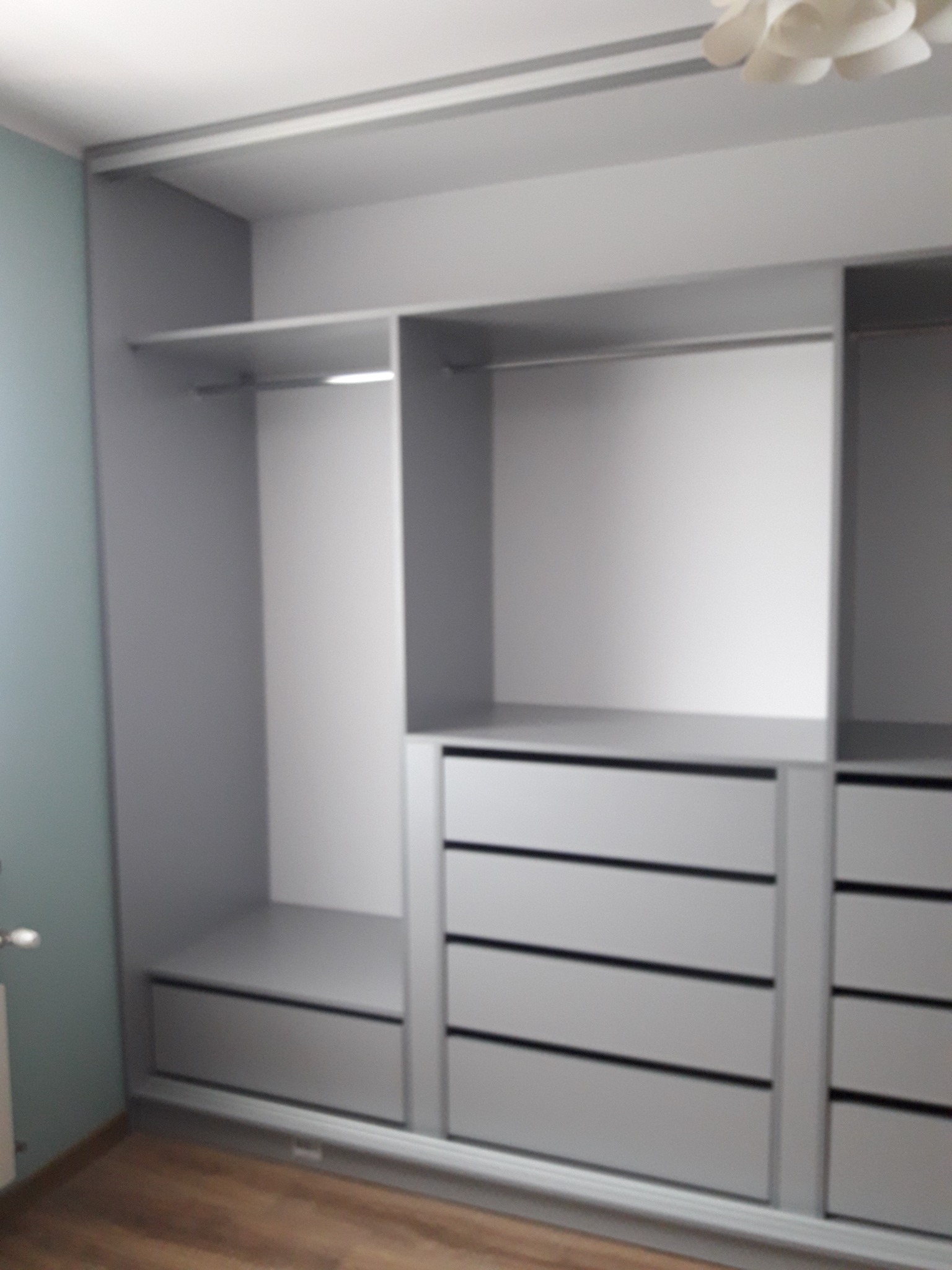 Szara, otwarta szafa wnękowa z półkami i szufladami, widoczna z perspektywy podłogi, oświetlona od góry.