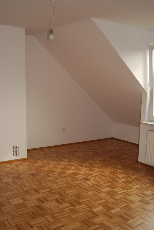 Pusty pokój na poddaszu z parkietem ułożonym w jodełkę, świeżo po cyklinowaniu, z widocznymi śladami po procesie na niektórych fragmentach podłogi.