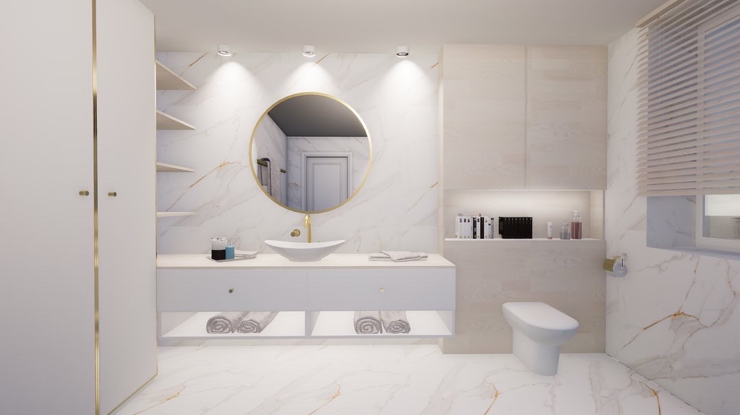 Elegancka łazienka z marmurowymi ścianami, okrągłym lustrem w złotej ramie, białą umywalką na blacie, podświetlanymi półkami z ręcznikami i toaletą.