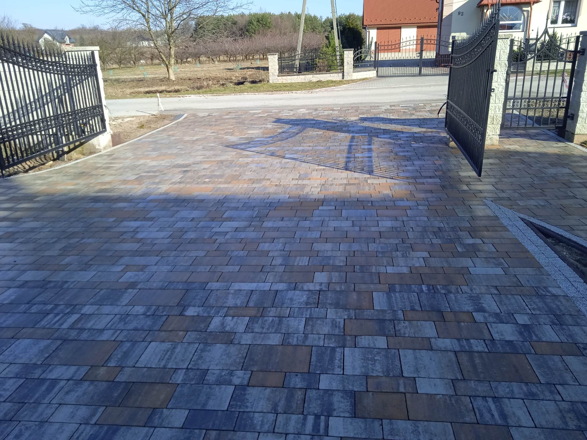 Ułożona, wielobarwna kostka brukowa na podjeździe w Chmielniku, z widocznymi cieniami bramy wjazdowej i fragmentem ulicy w tle.