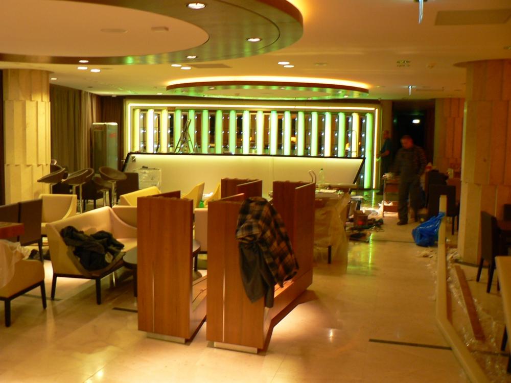 Wnętrze lokalu gastronomicznego w trakcie montażu oświetlenia baru. Widoczne meble i elementy dekoracyjne w ciepłej kolorystyce.